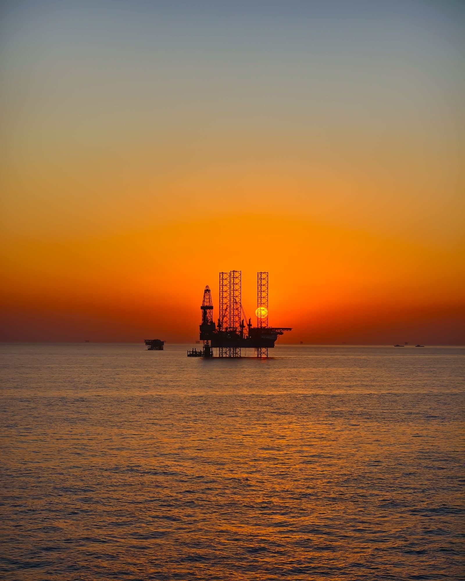 Offshore jack-up rig and support vessel at sunset